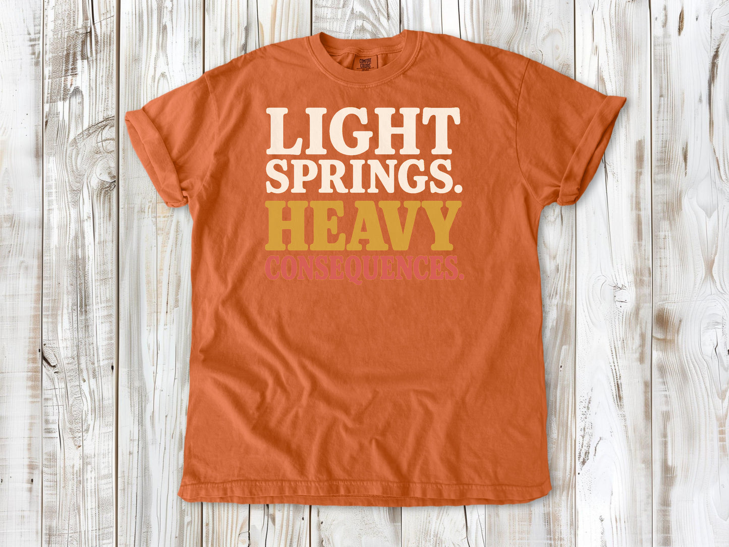 Burnt Orange garment-dyed tee with Light Springs Heavy Consequences reformer Pilates graphic.