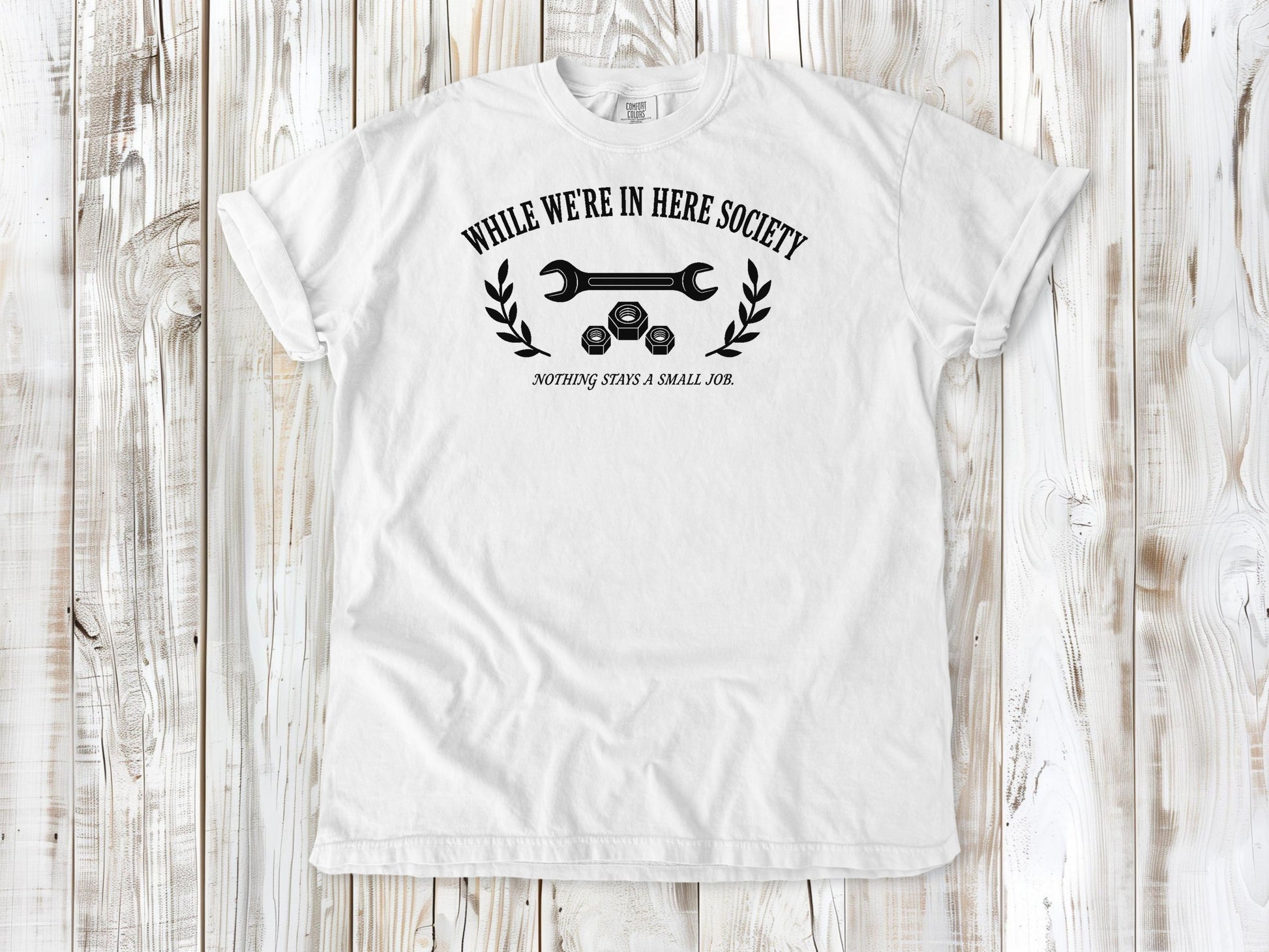 White garment-dyed tee with While We're in Here Society garage humor graphic.