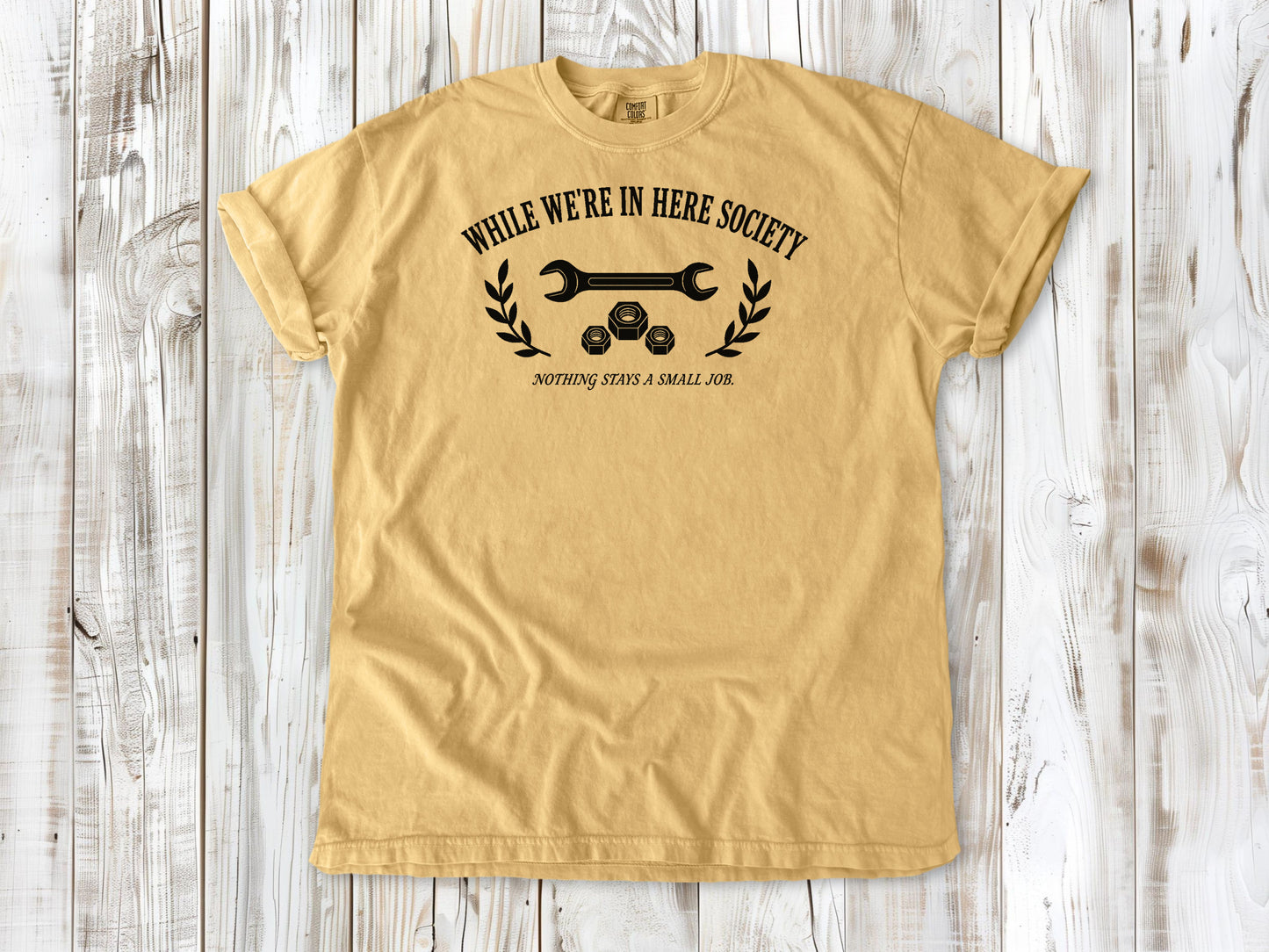 Mustard garment-dyed tee with While We're in Here Society garage humor graphic.
