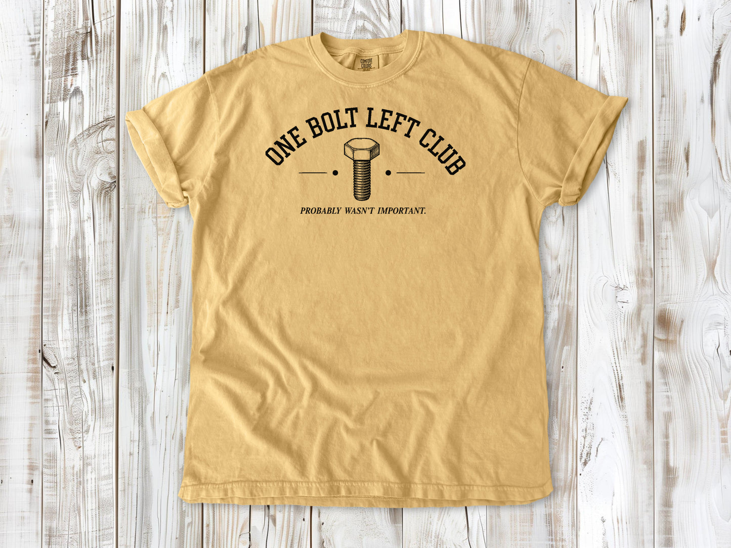 Mustard garment-dyed tee with One Bolt Left Club mechanic humor graphic.