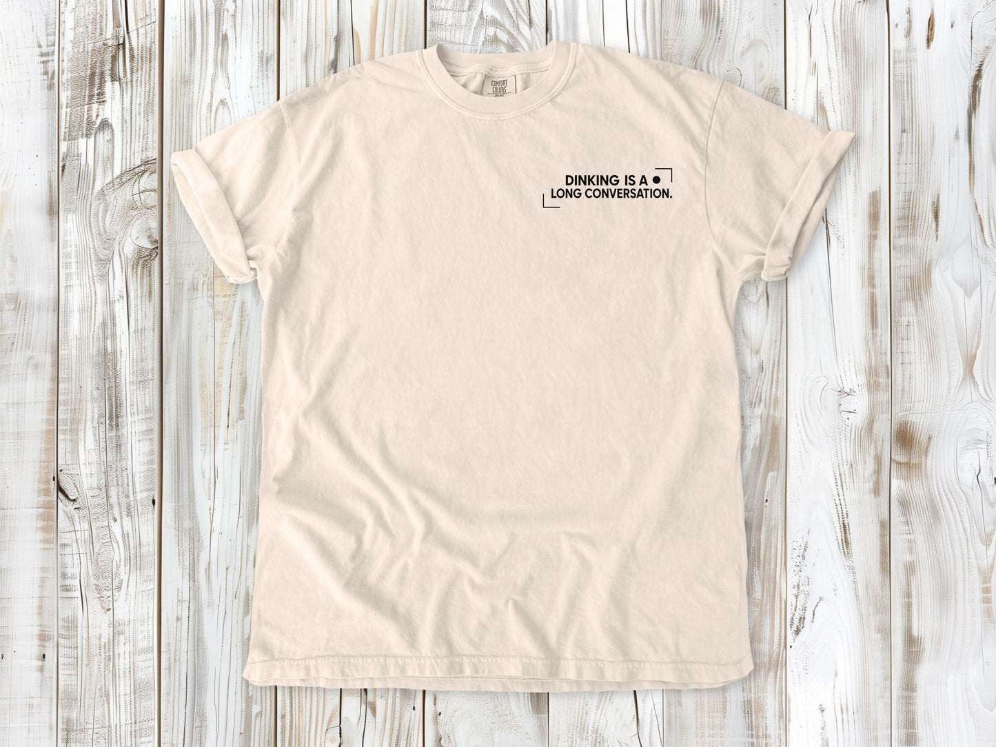 Ivory garment-dyed tee with Dinking Is a Long Conversation small left-chest pickleball graphic.