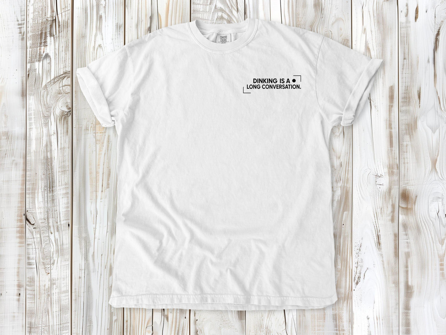 White garment-dyed tee with Dinking Is a Long Conversation small left-chest pickleball graphic.