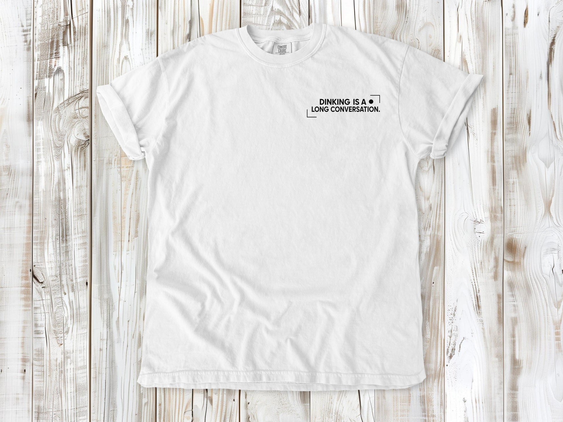 White garment-dyed tee with Dinking Is a Long Conversation small left-chest pickleball graphic.