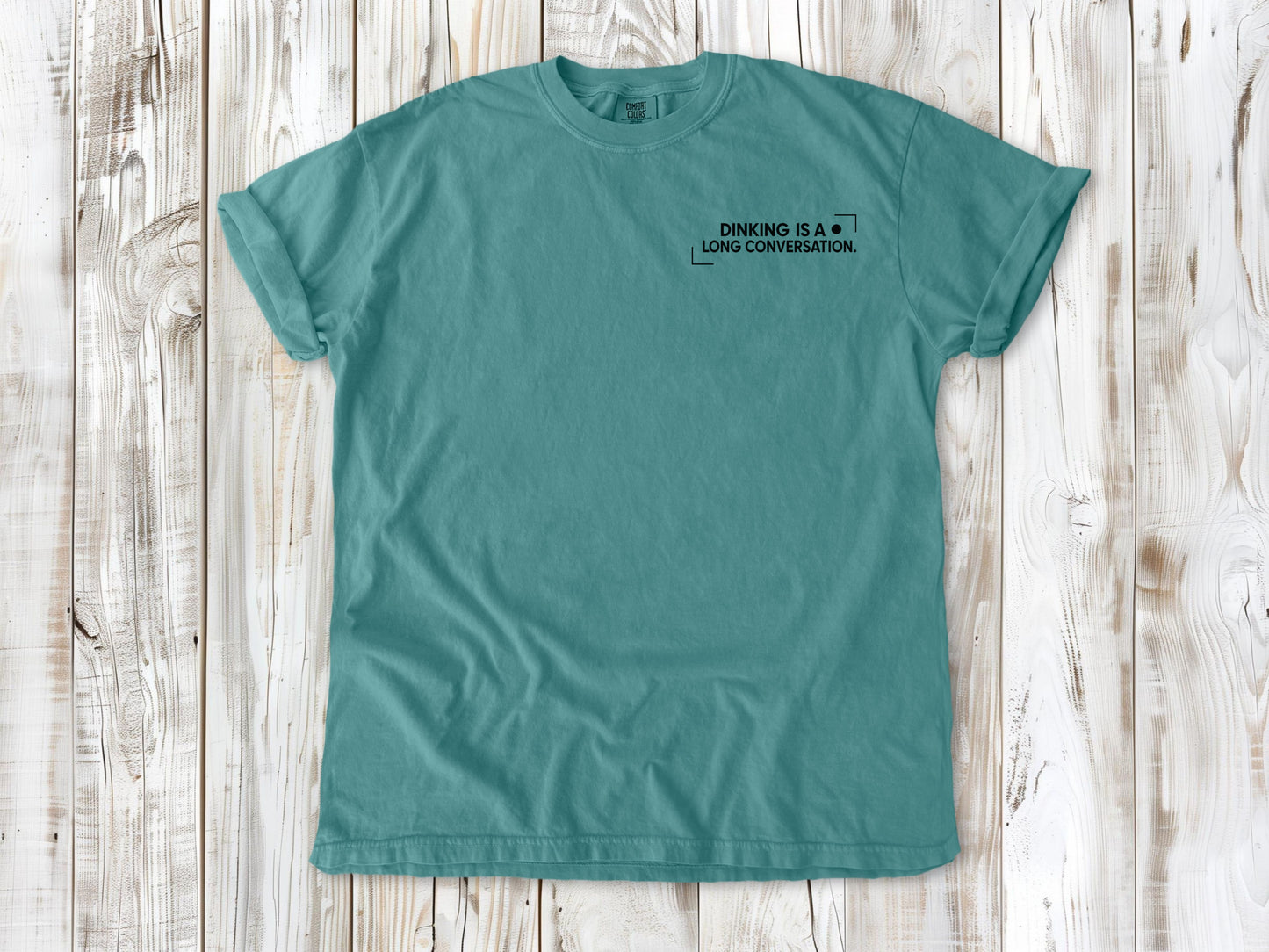 Seafoam garment-dyed tee with Dinking Is a Long Conversation small left-chest pickleball graphic.