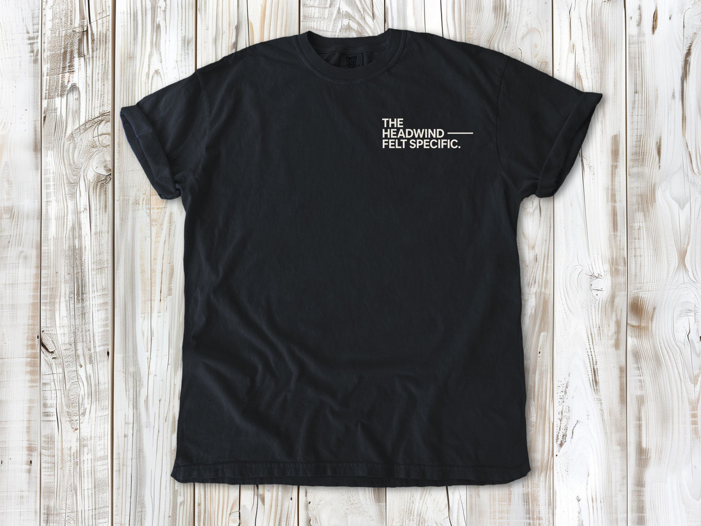 Graphite garment-dyed tee with The Headwind Felt Specific small left-chest cycling graphic.