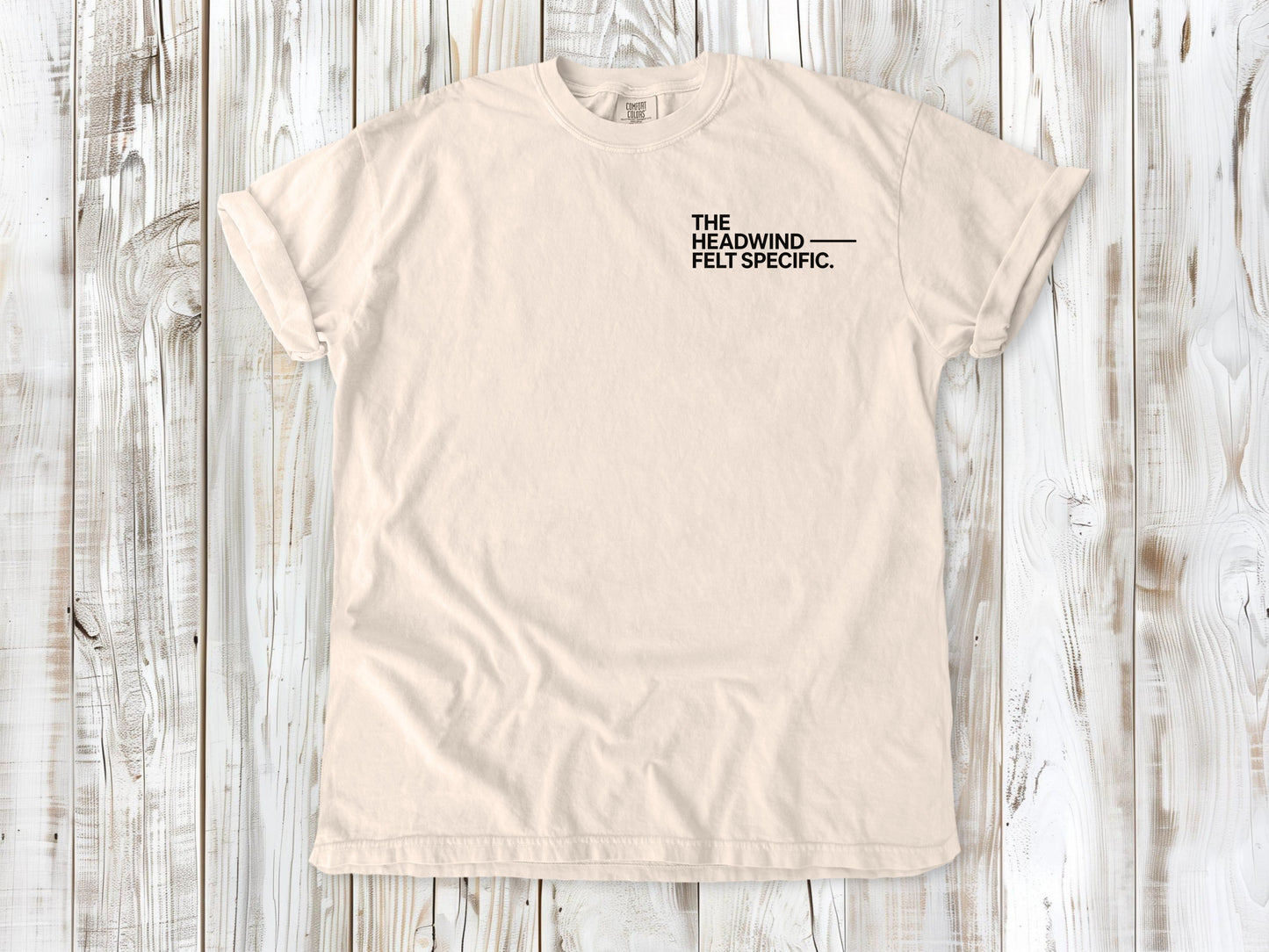 Ivory garment-dyed tee with The Headwind Felt Specific small left-chest cycling graphic.