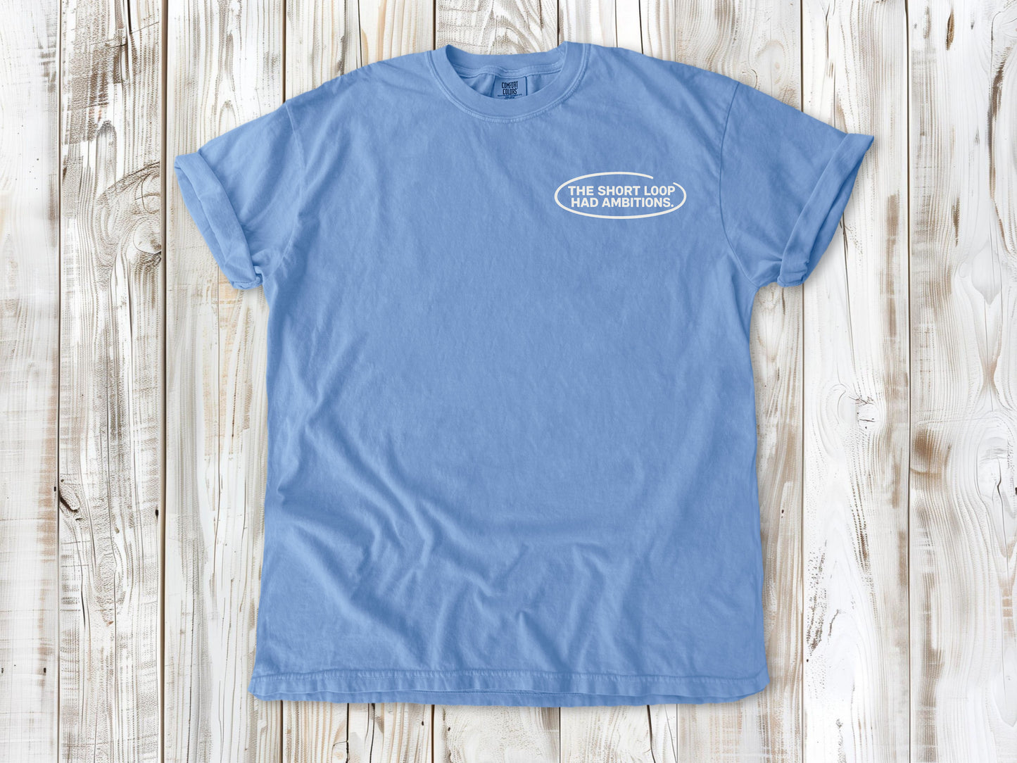 Washed Denim garment-dyed tee with The Short Loop Had Ambitions small left-chest cycling graphic.