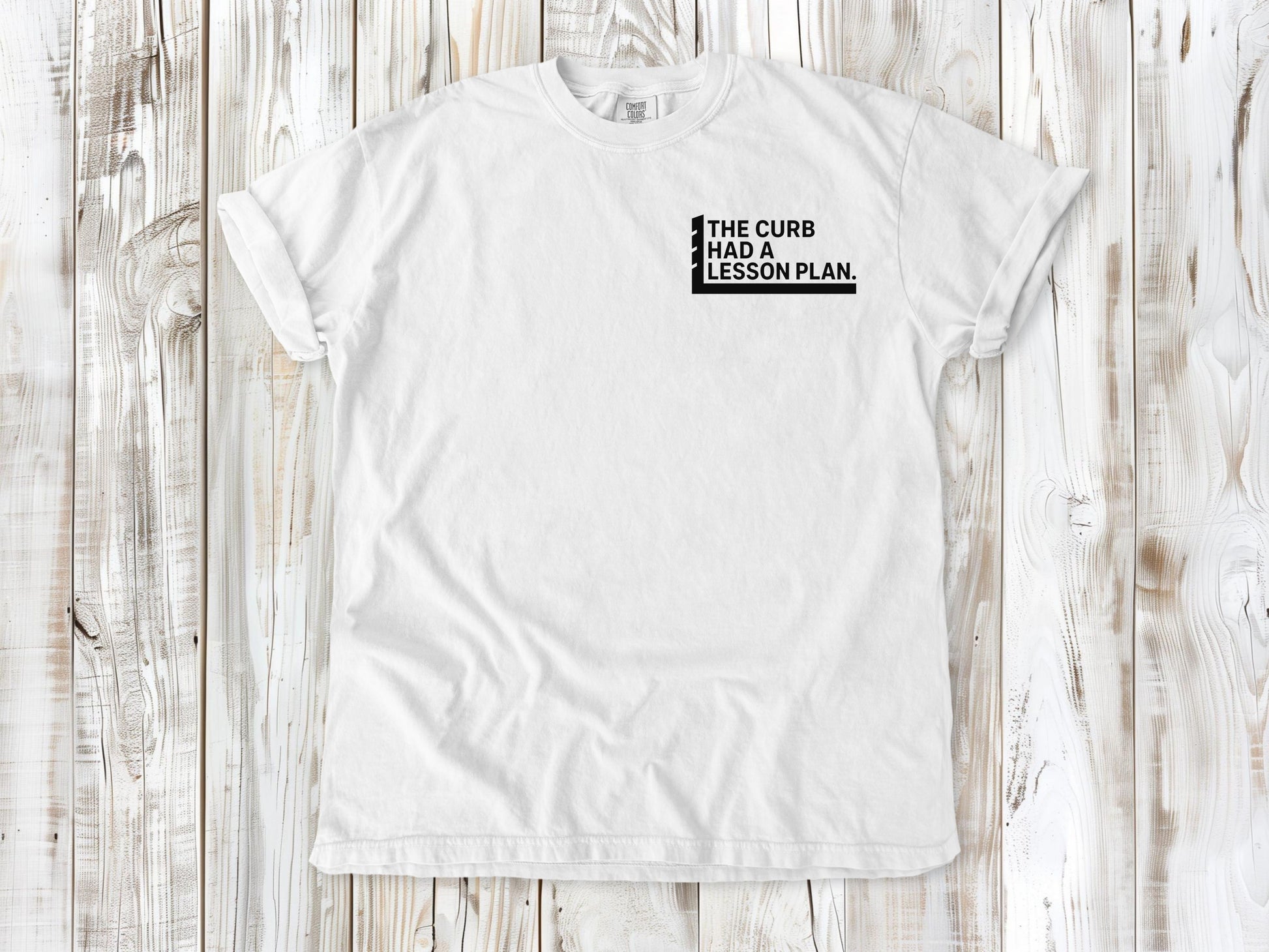 White garment-dyed tee with The Curb Had a Lesson Plan small left-chest skate graphic.
