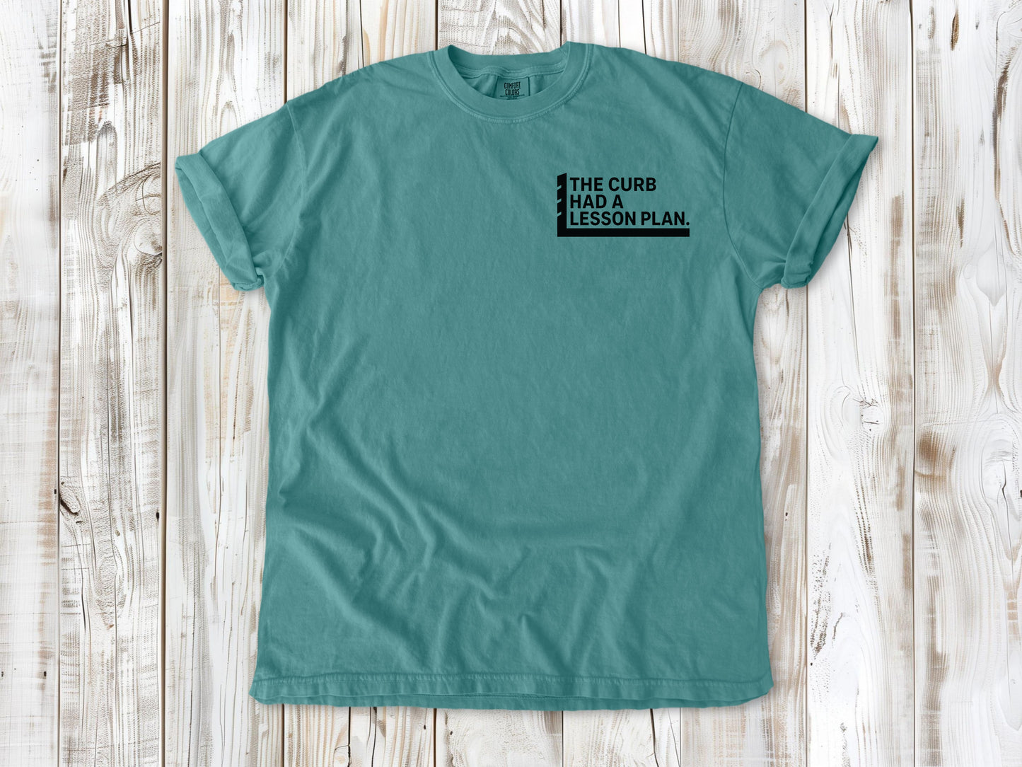 Seafoam garment-dyed tee with The Curb Had a Lesson Plan small left-chest skate graphic.