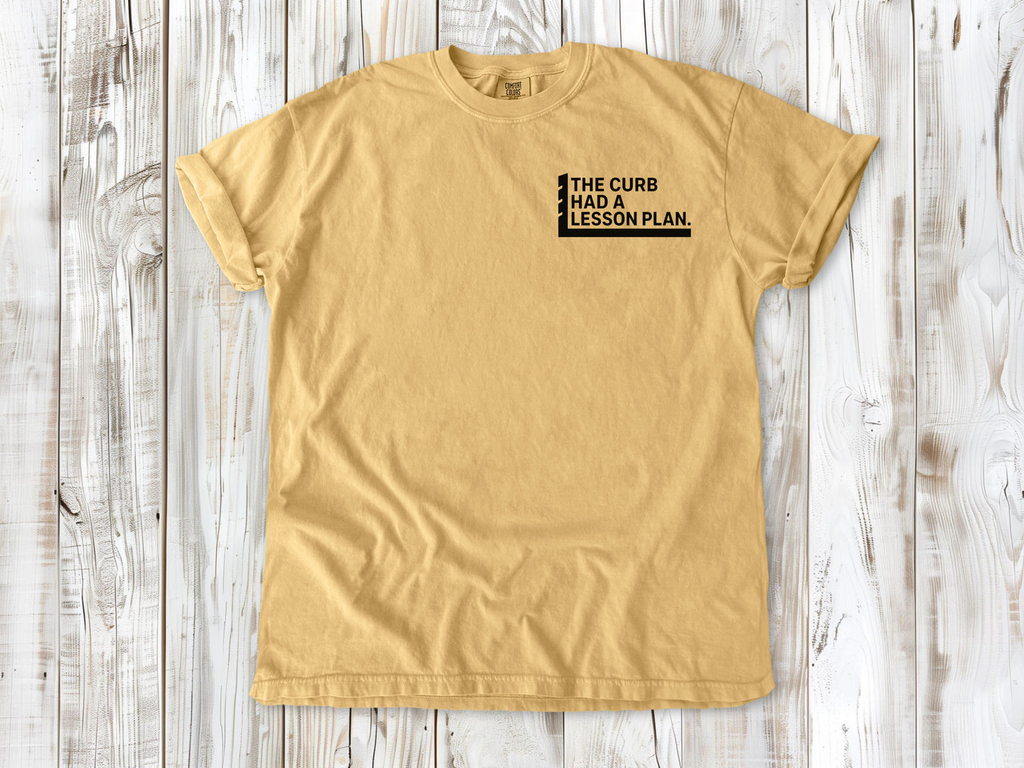 Mustard garment-dyed tee with The Curb Had a Lesson Plan small left-chest skate graphic.
