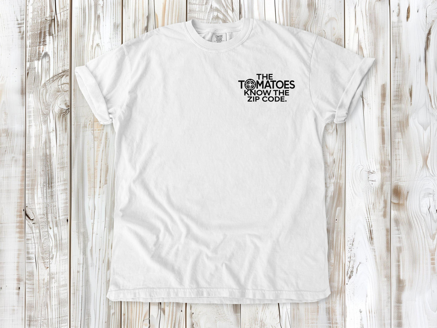 White garment-dyed tee with The Tomatoes Know the Zip Code small left-chest gardening graphic.