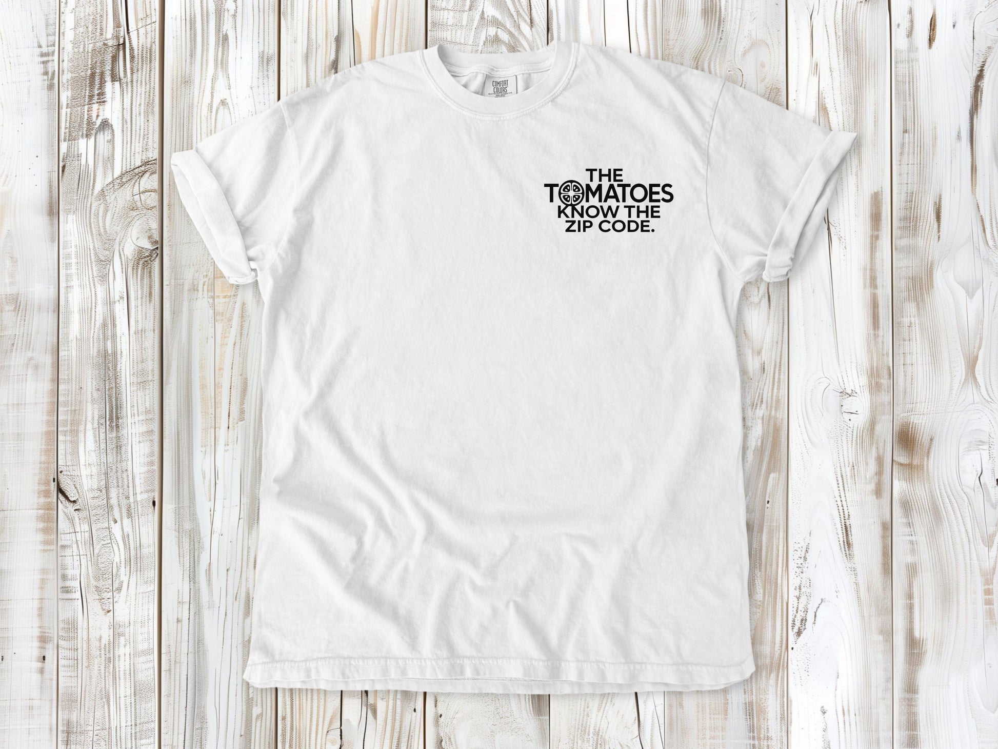 White garment-dyed tee with The Tomatoes Know the Zip Code small left-chest gardening graphic.