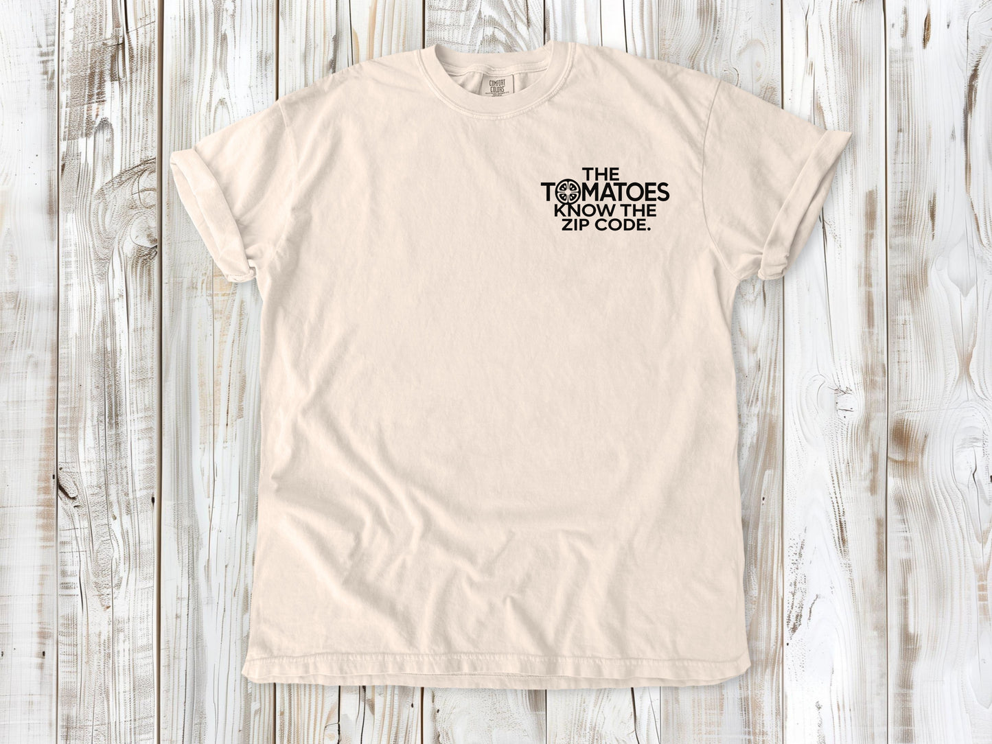 Ivory garment-dyed tee with The Tomatoes Know the Zip Code small left-chest gardening graphic.