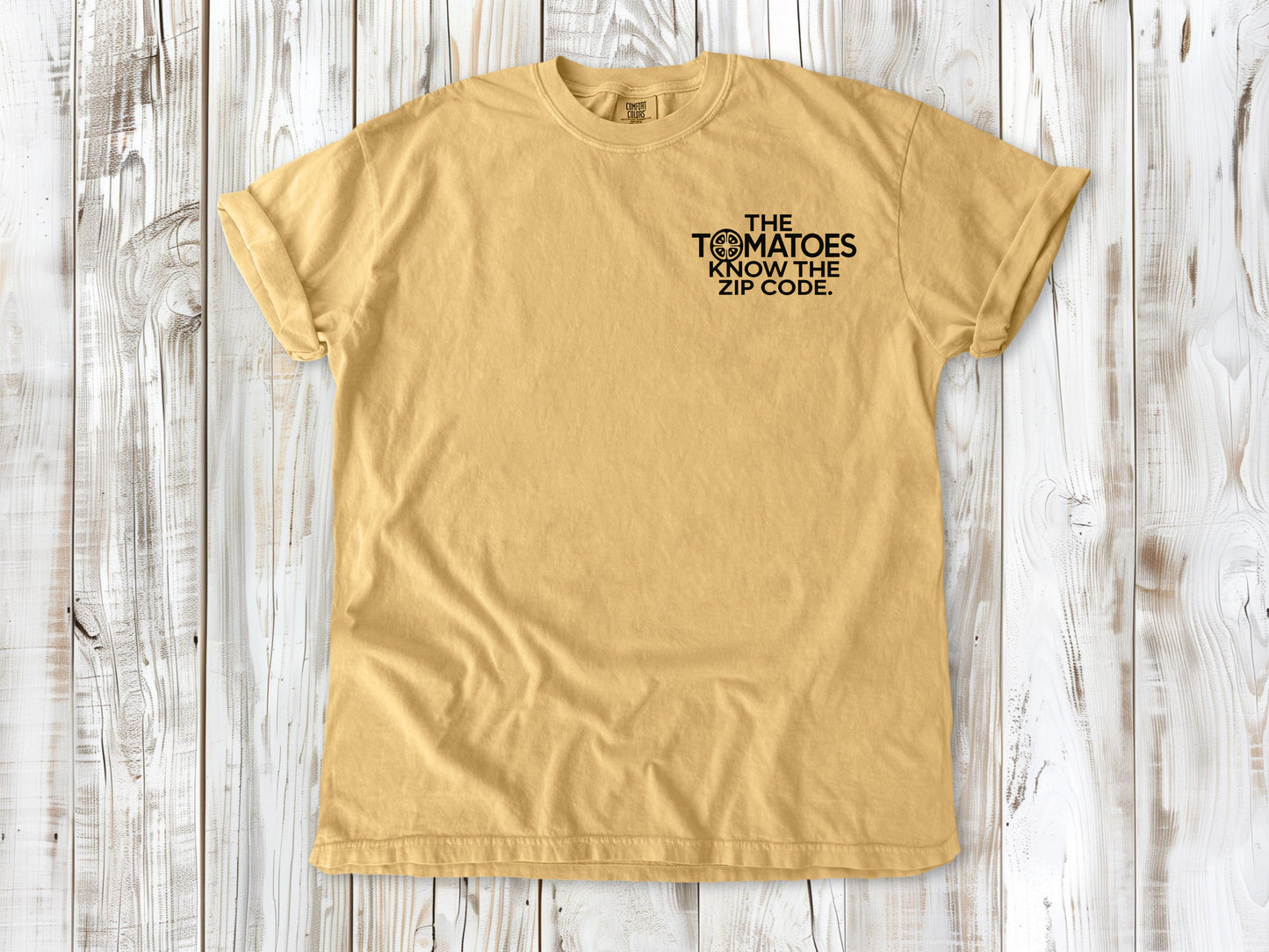 Mustard garment-dyed tee with The Tomatoes Know the Zip Code small left-chest gardening graphic.