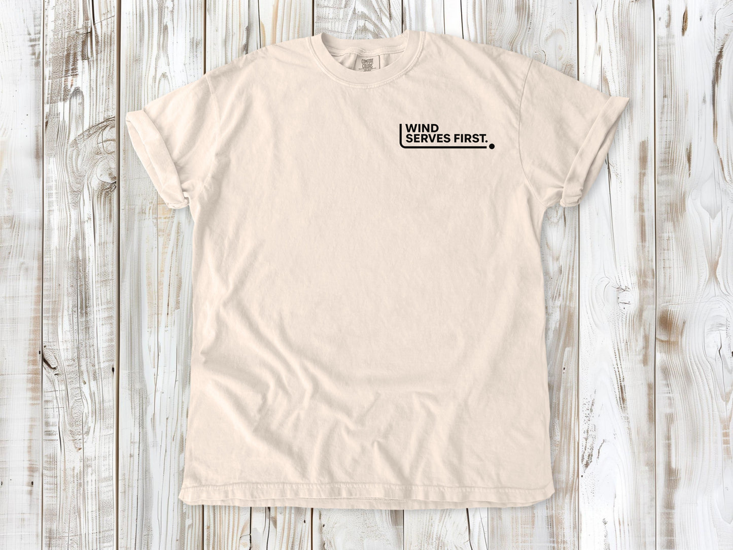 Ivory garment-dyed tee with Wind Serves First small left-chest beach volleyball graphic.