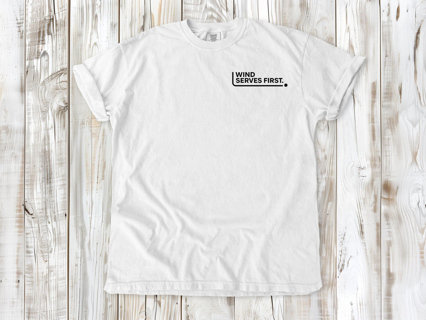 White garment-dyed tee with Wind Serves First small left-chest beach volleyball graphic.