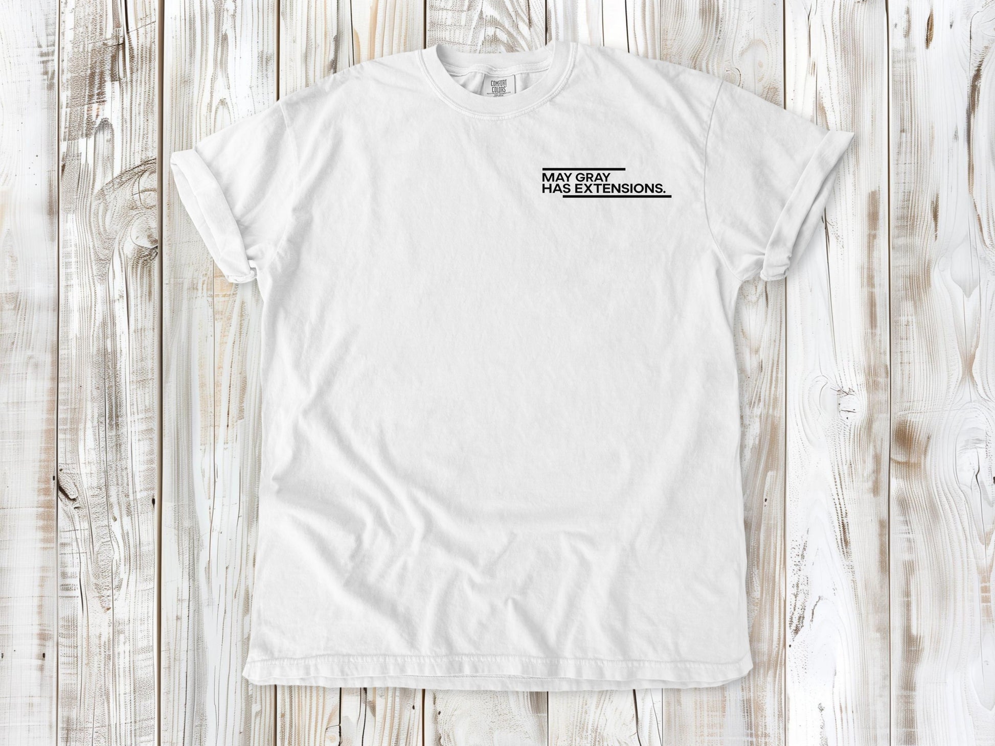 White garment-dyed tee with May Gray Has Extensions small left-chest coastal graphic.
