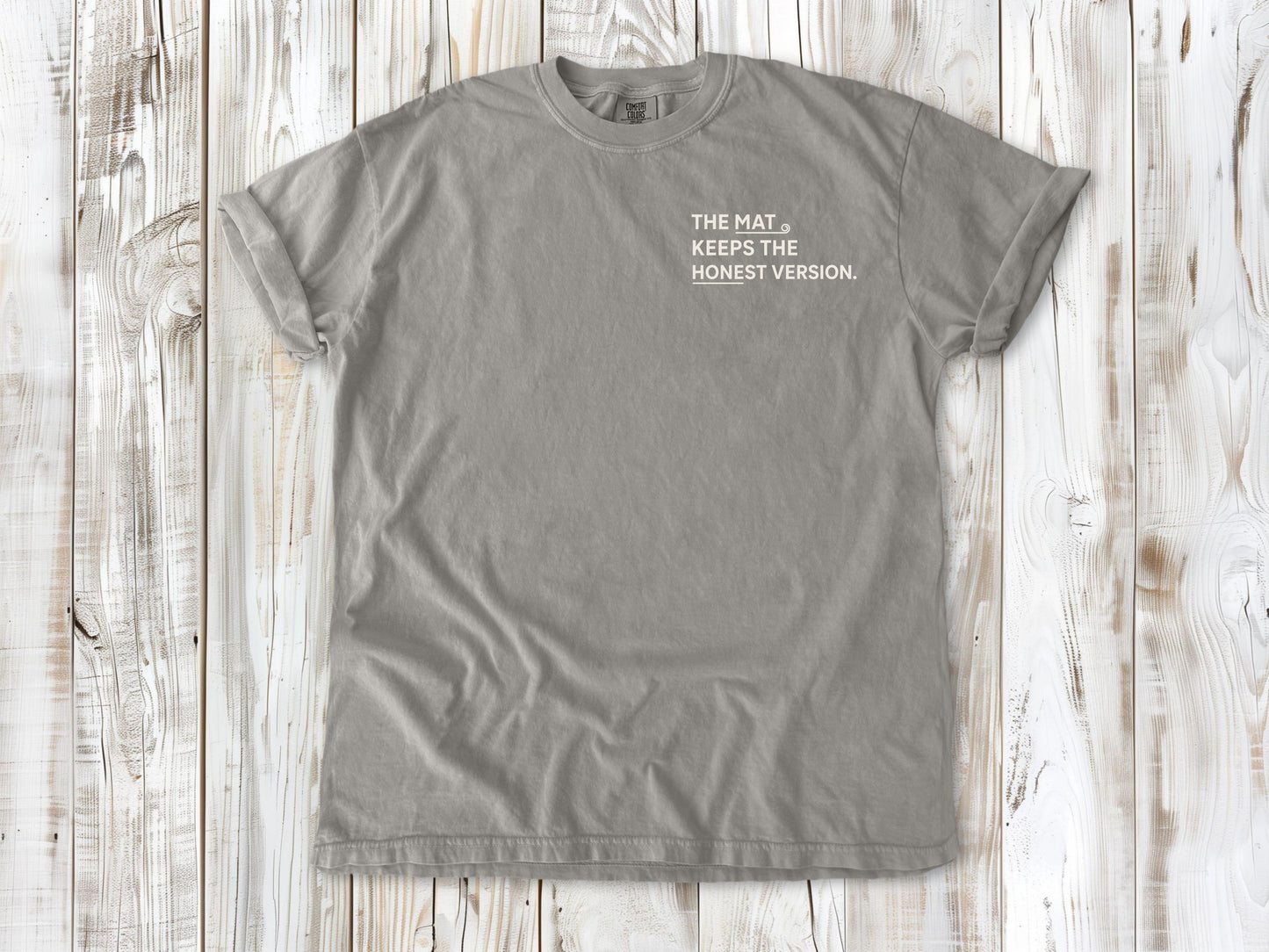 Grey garment-dyed tee with The Mat Keeps the Honest Version small left-chest yoga graphic.