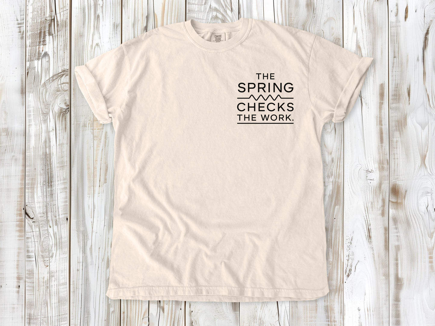 Ivory garment-dyed tee with The Spring Checks the Work small left-chest Pilates graphic.