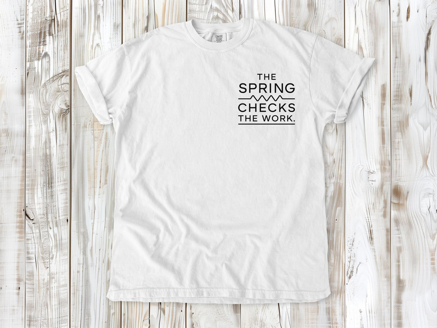White garment-dyed tee with The Spring Checks the Work small left-chest Pilates graphic.