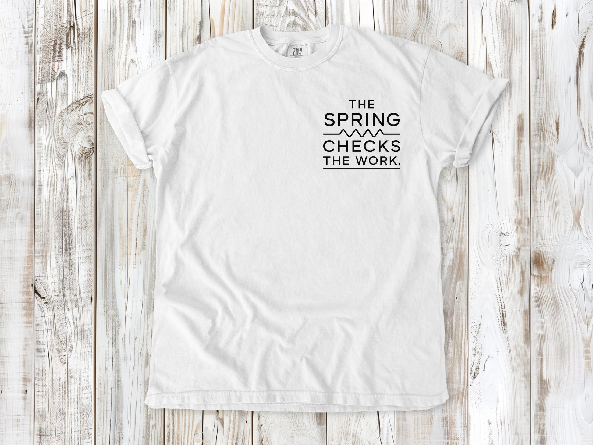 White garment-dyed tee with The Spring Checks the Work small left-chest Pilates graphic.