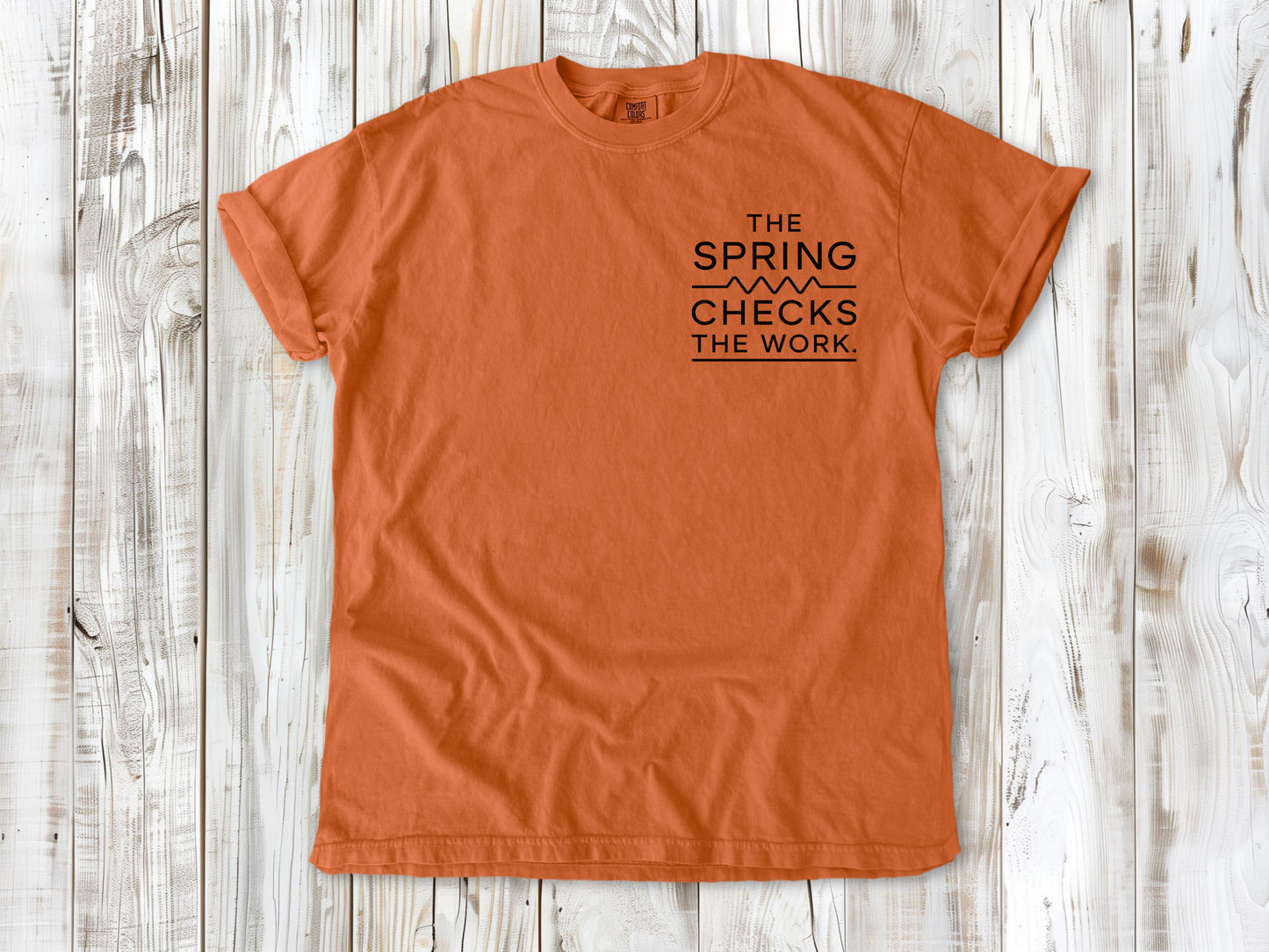 Burnt Orange garment-dyed tee with The Spring Checks the Work small left-chest Pilates graphic.