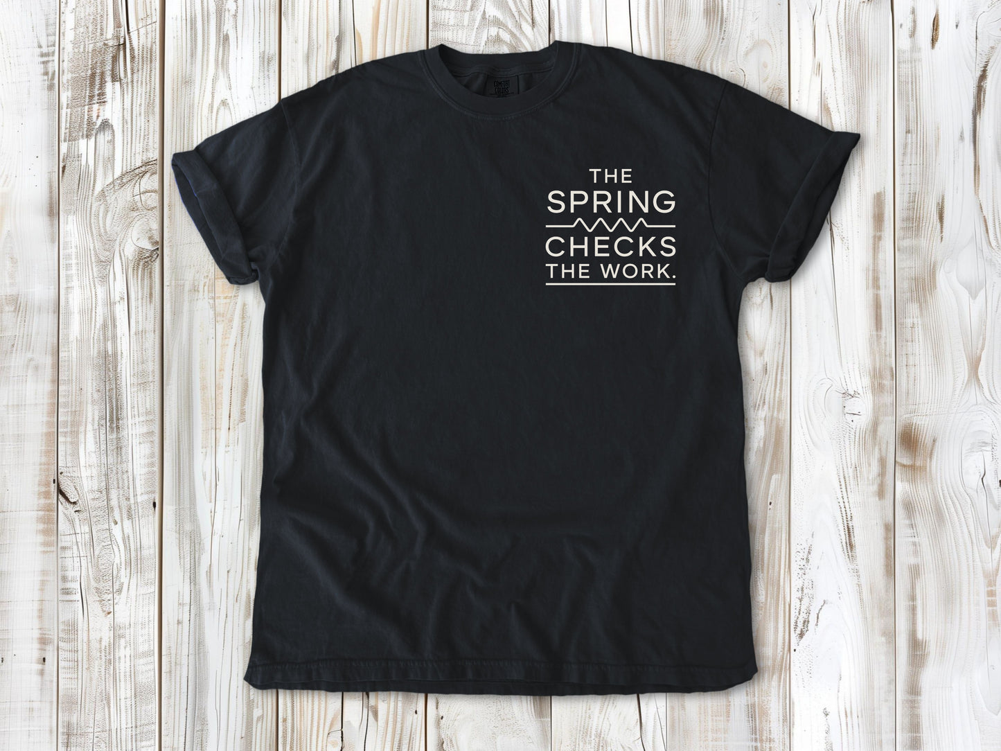 Graphite garment-dyed tee with The Spring Checks the Work small left-chest Pilates graphic.