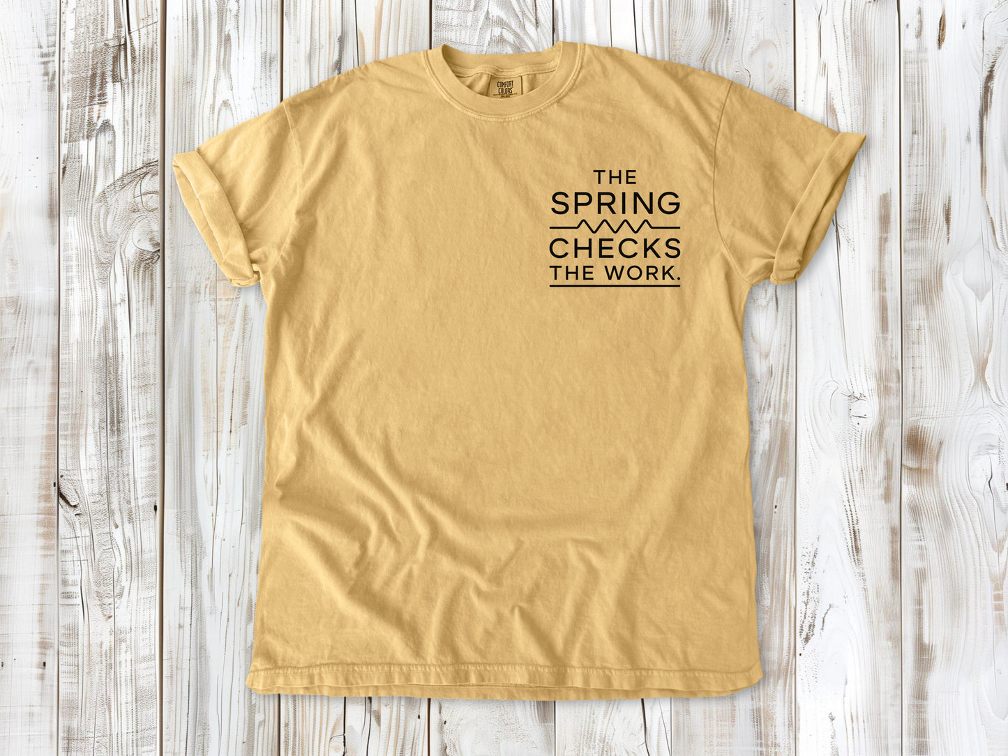 Mustard garment-dyed tee with The Spring Checks the Work small left-chest Pilates graphic.