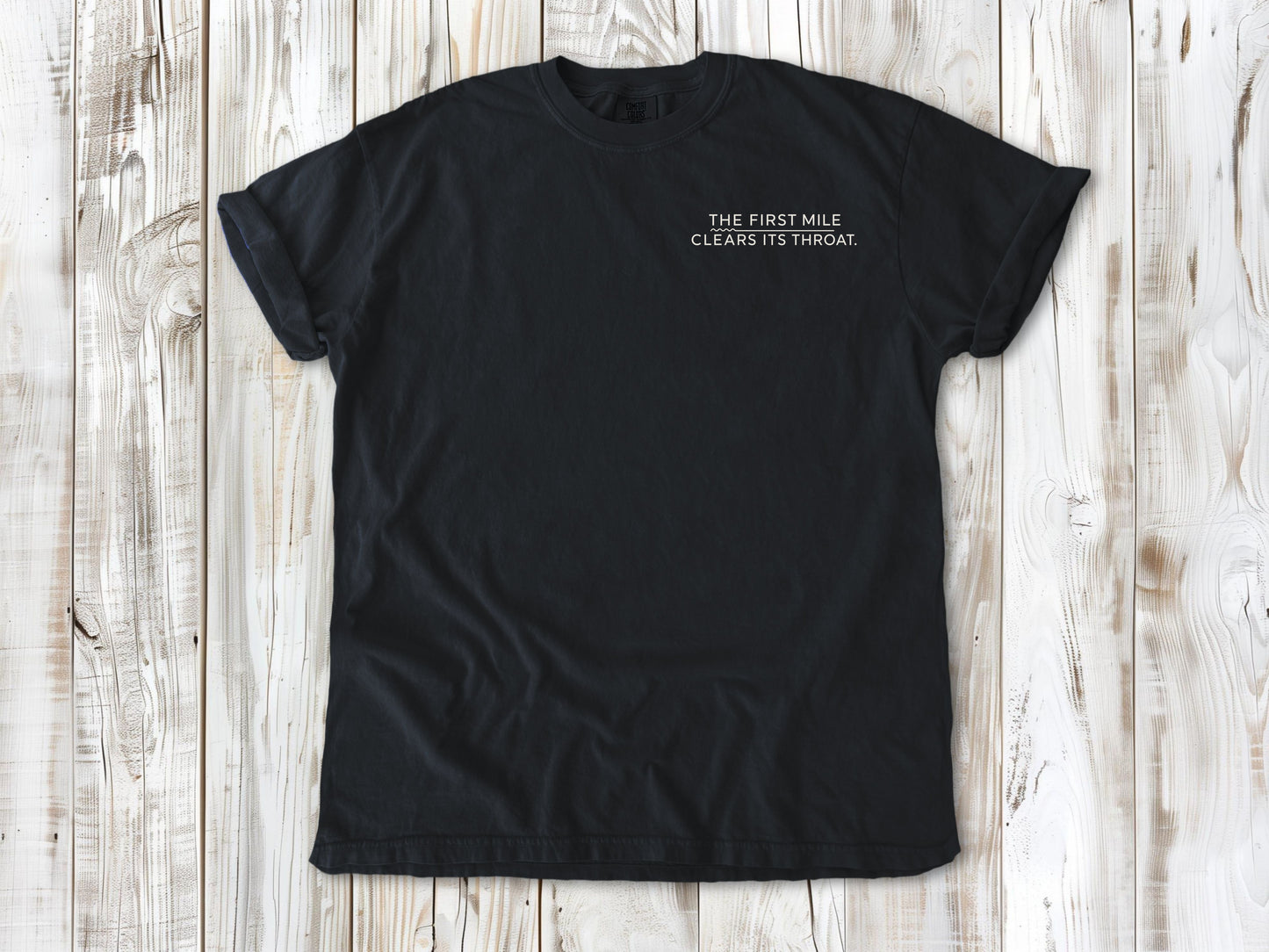 Graphite garment-dyed tee with The First Mile Clears Its Throat small left-chest running graphic.