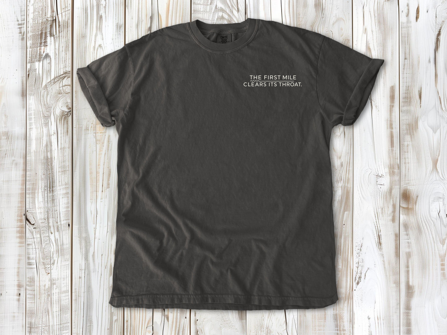 Pepper garment-dyed tee with The First Mile Clears Its Throat small left-chest running graphic.