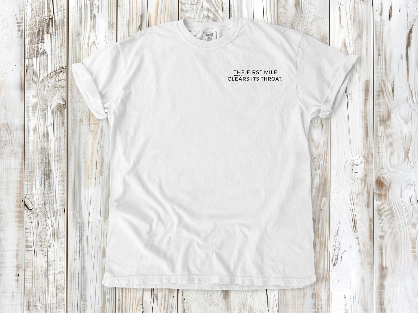 White garment-dyed tee with The First Mile Clears Its Throat small left-chest running graphic.