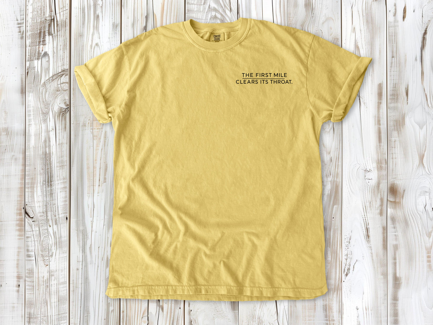 Butter garment-dyed tee with The First Mile Clears Its Throat small left-chest running graphic.