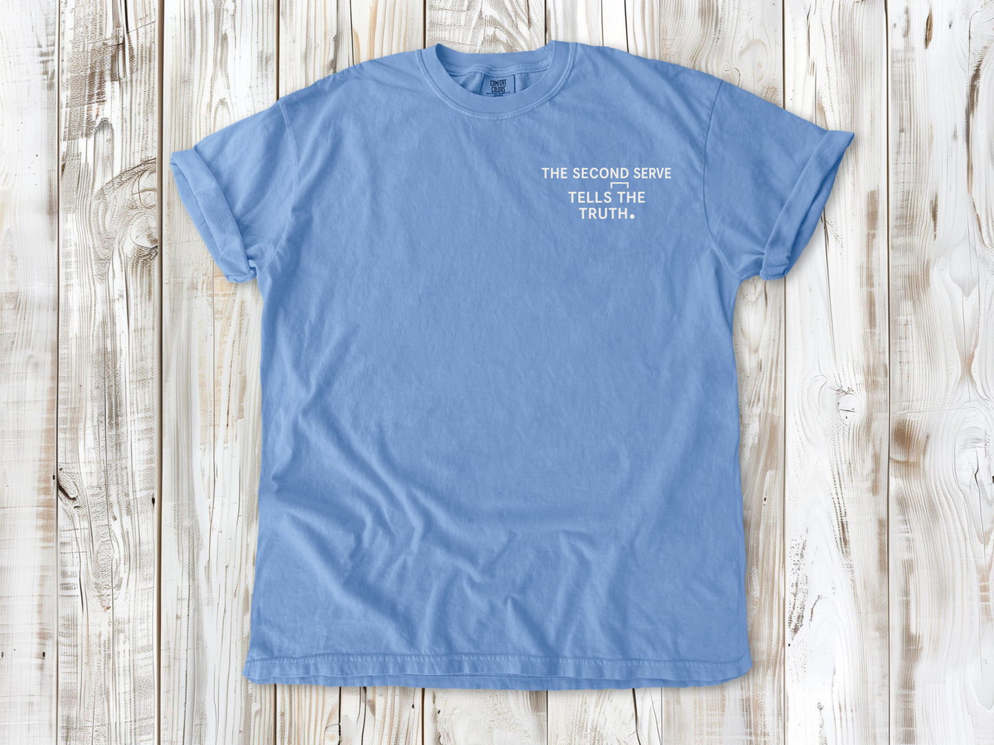 Washed Denim garment-dyed tee with The Second Serve Tells the Truth small left-chest tennis graphic.