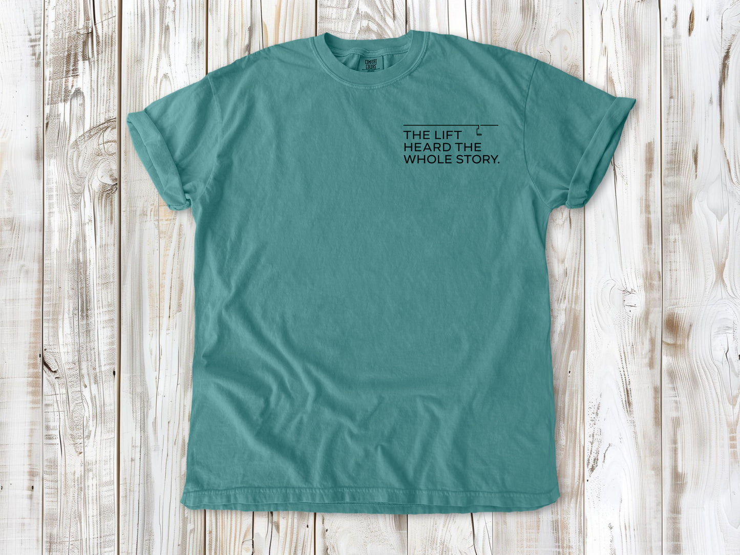 Seafoam garment-dyed tee with The Lift Heard the Whole Story small left-chest snowboarding graphic.