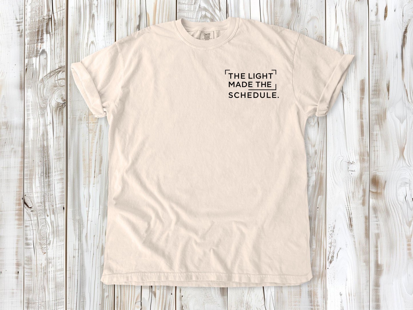 Ivory garment-dyed tee with The Light Made the Schedule small left-chest photography graphic.