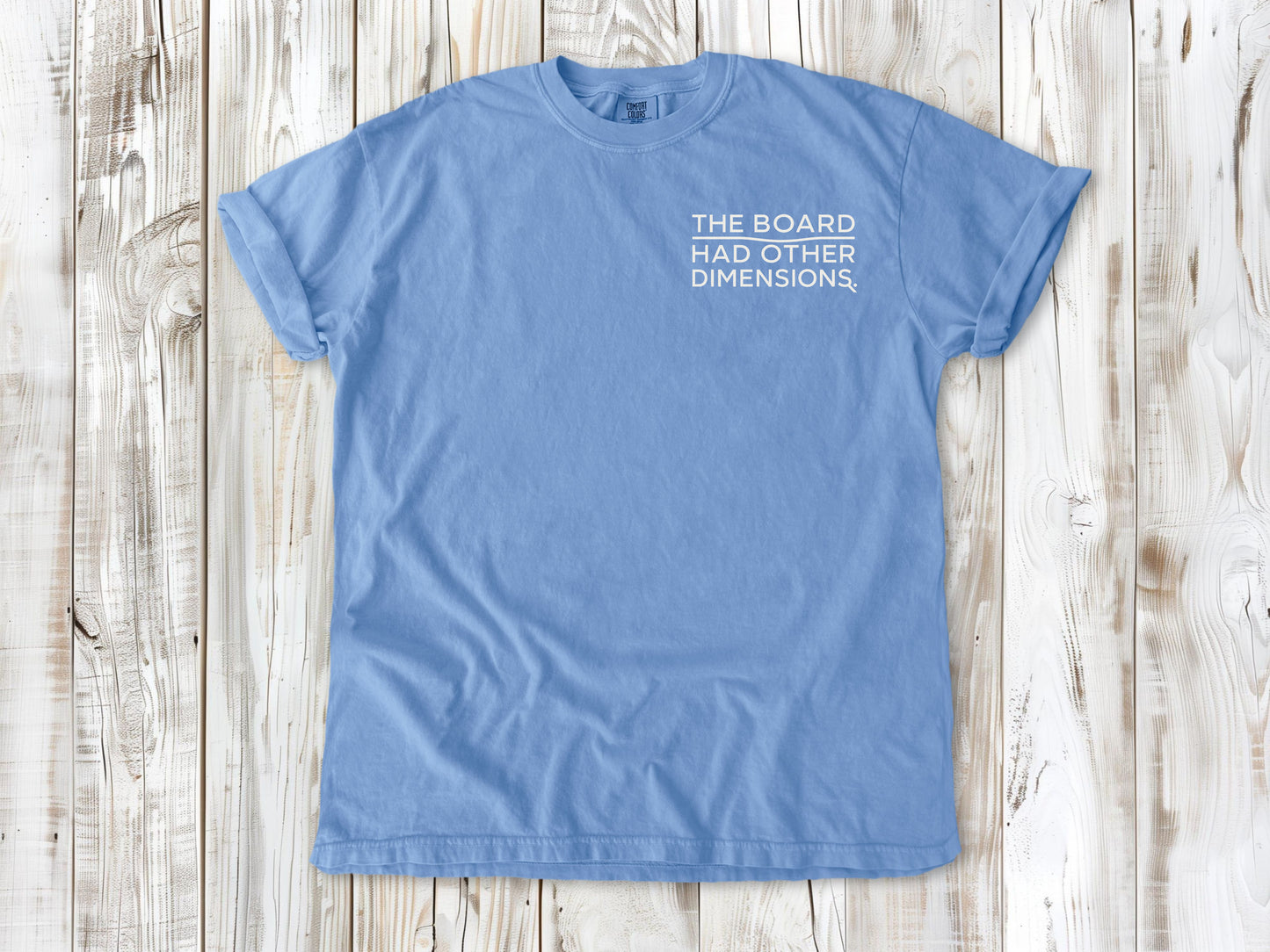 Washed Denim garment-dyed tee with The Board Had Other Dimensions small left-chest woodworking graphic.