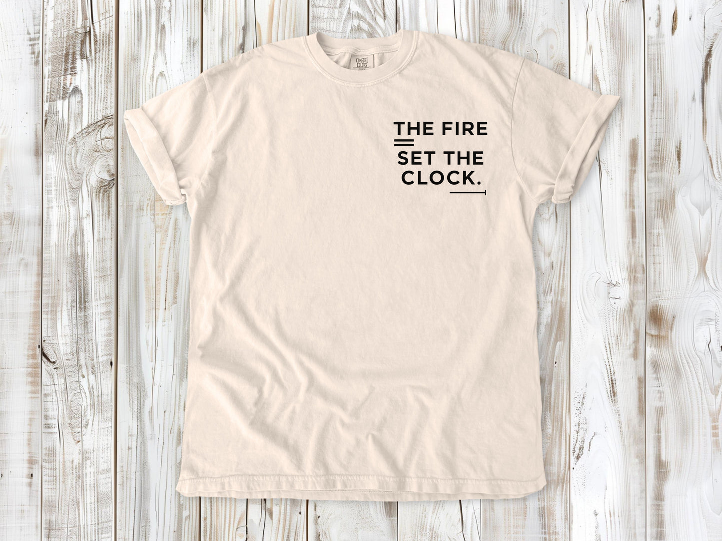 Ivory garment-dyed tee with The Fire Set the Clock small left-chest camping graphic.