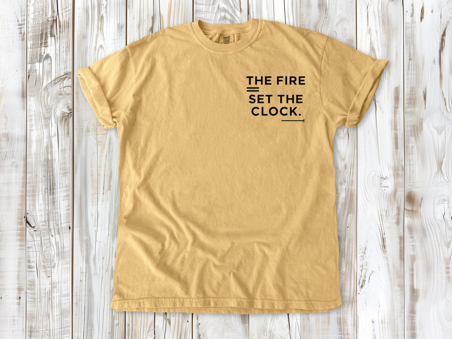 Mustard garment-dyed tee with The Fire Set the Clock small left-chest camping graphic.