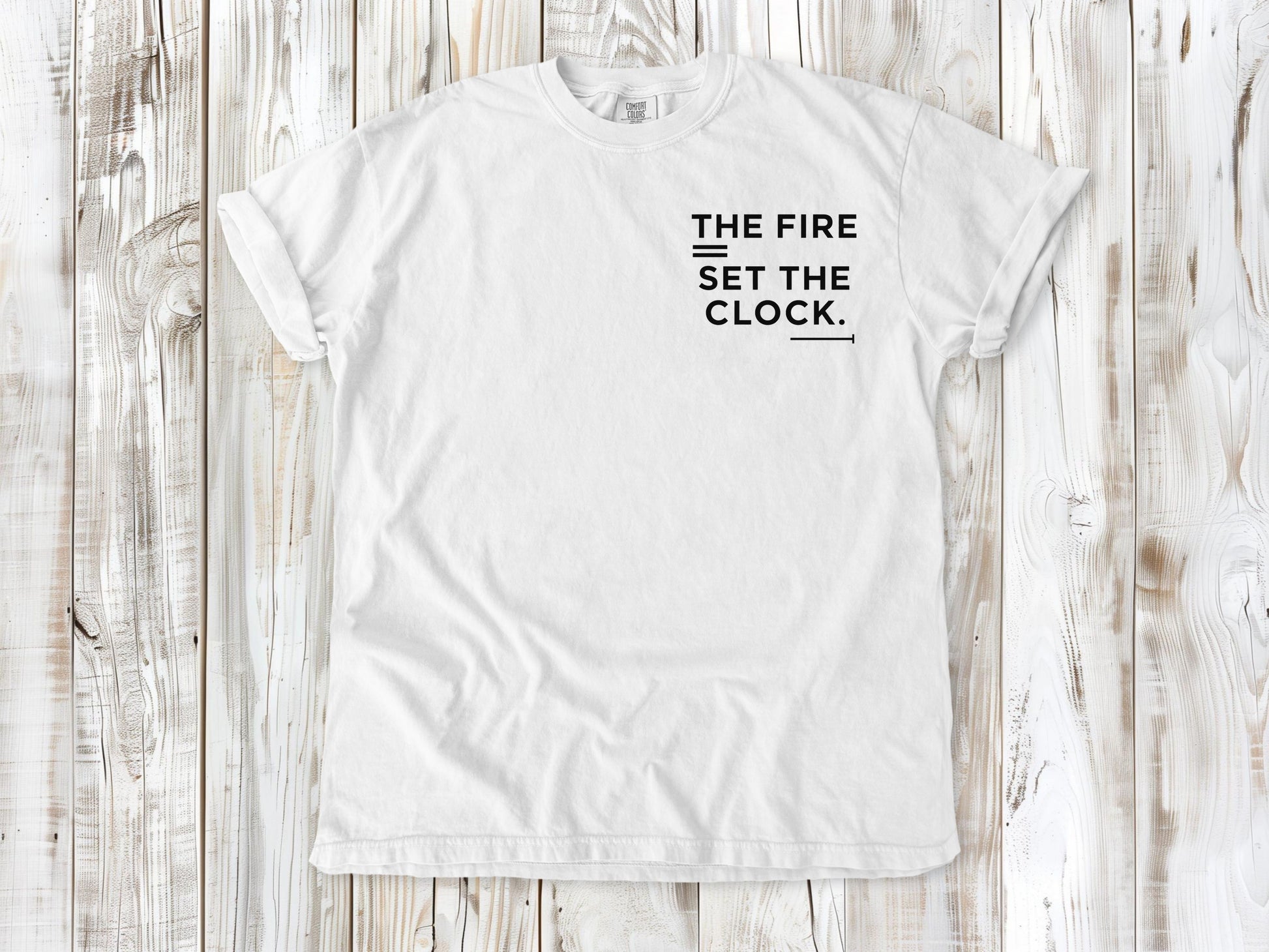 White garment-dyed tee with The Fire Set the Clock small left-chest camping graphic.