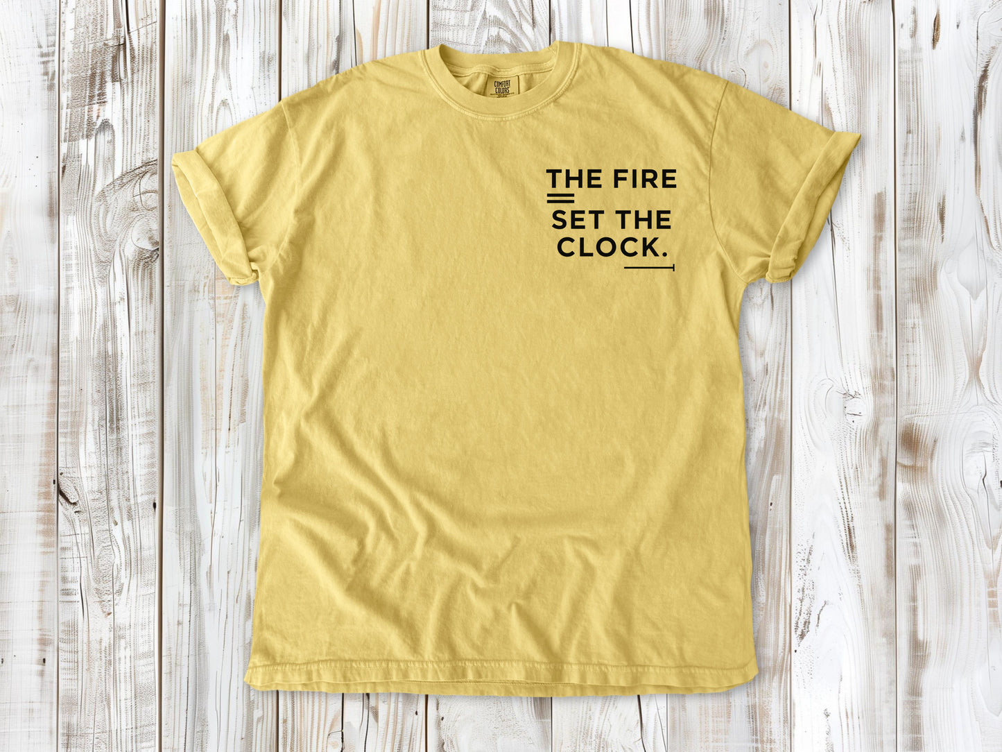 Butter garment-dyed tee with The Fire Set the Clock small left-chest camping graphic.