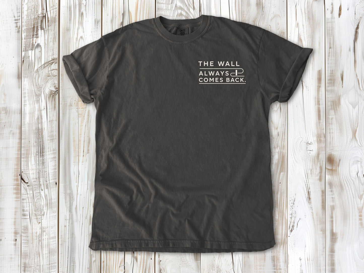 Pepper garment-dyed tee with The Wall Always Comes Back small left-chest swimming graphic.