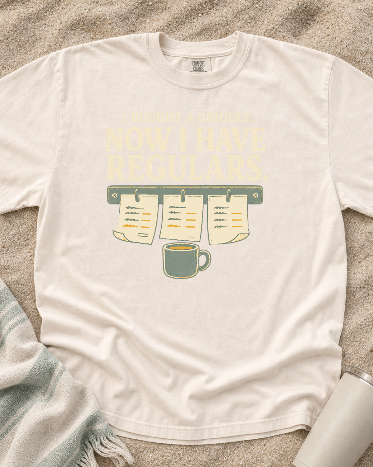 Ivory garment-dyed tee with I Bought a Griddle Now I Have Regulars graphic.
