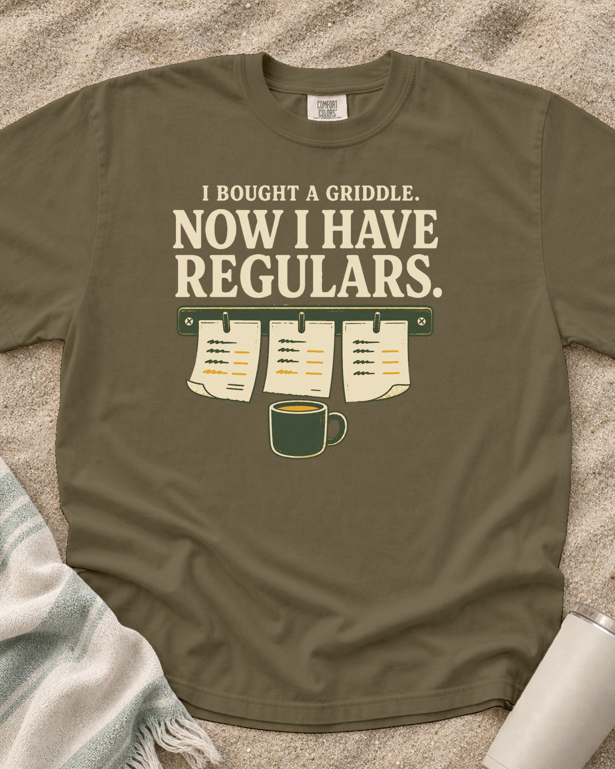 Khaki garment-dyed tee with I Bought a Griddle Now I Have Regulars graphic.