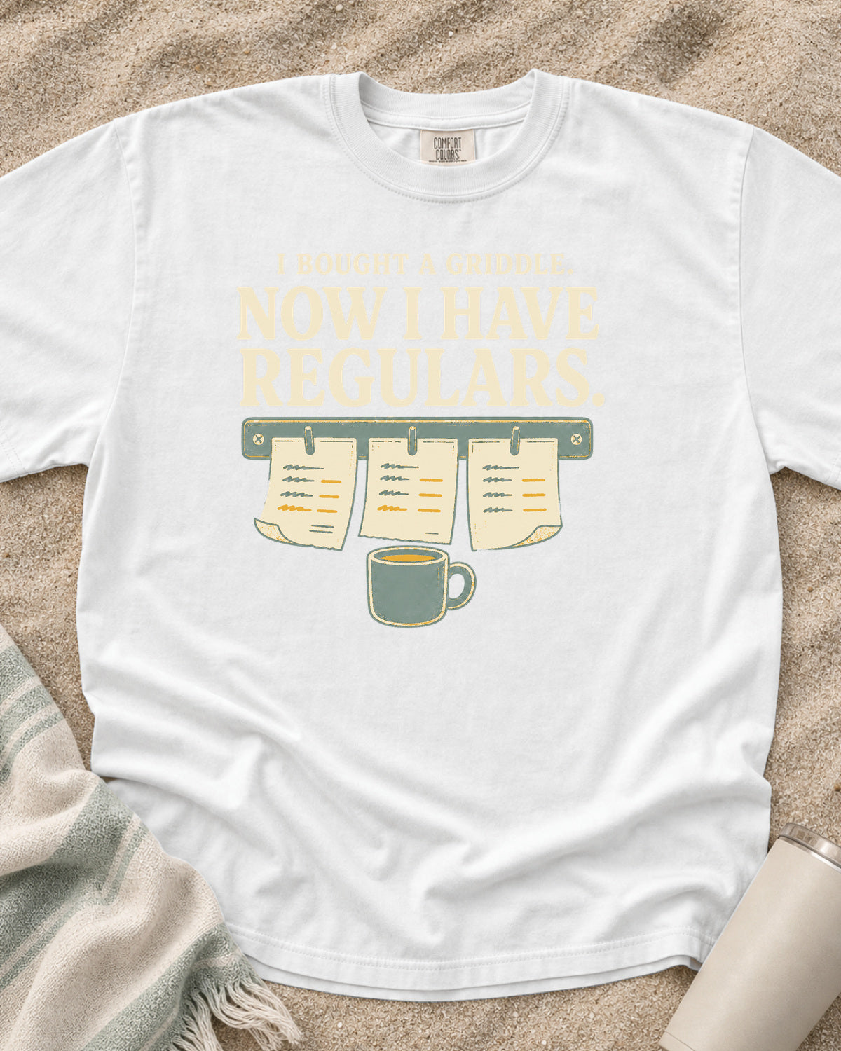 White garment-dyed tee with I Bought a Griddle Now I Have Regulars graphic.