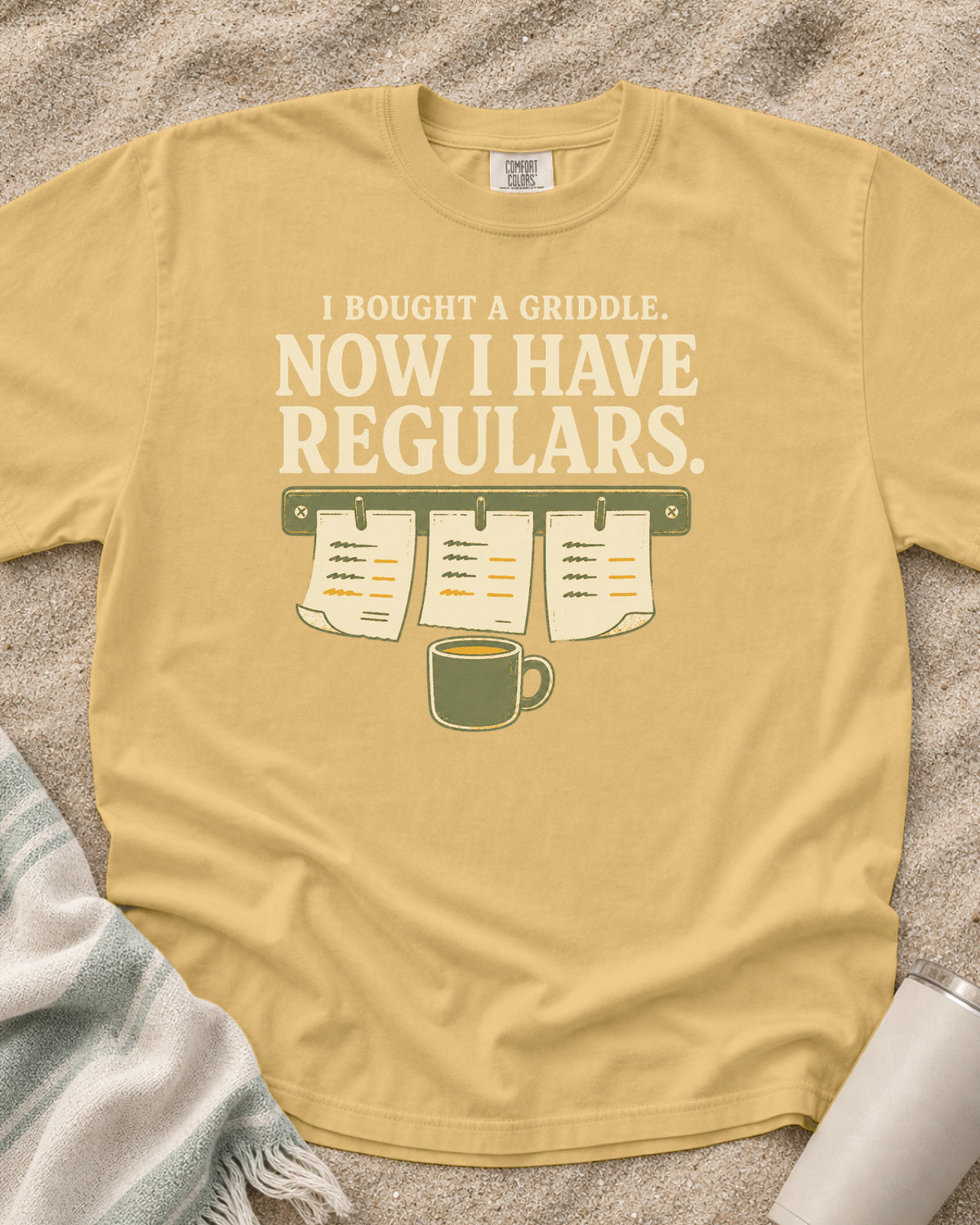 Mustard garment-dyed tee with I Bought a Griddle Now I Have Regulars graphic.
