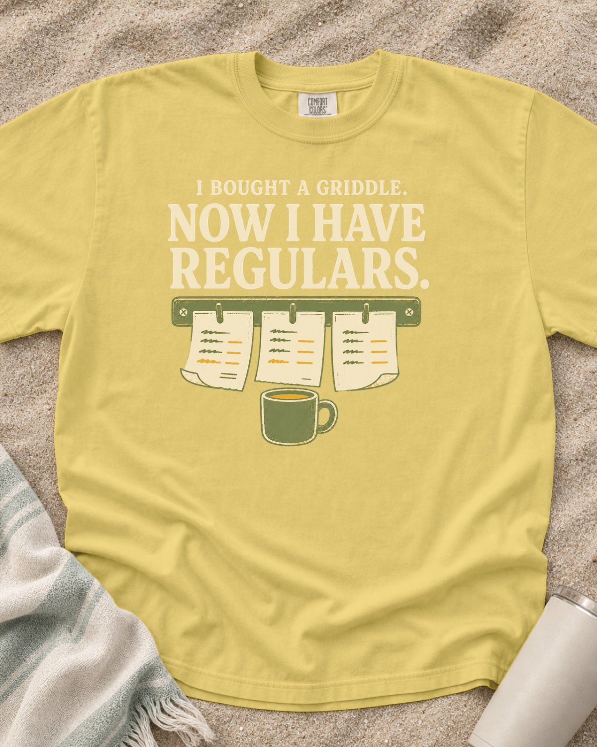 Butter garment-dyed tee with I Bought a Griddle Now I Have Regulars graphic.