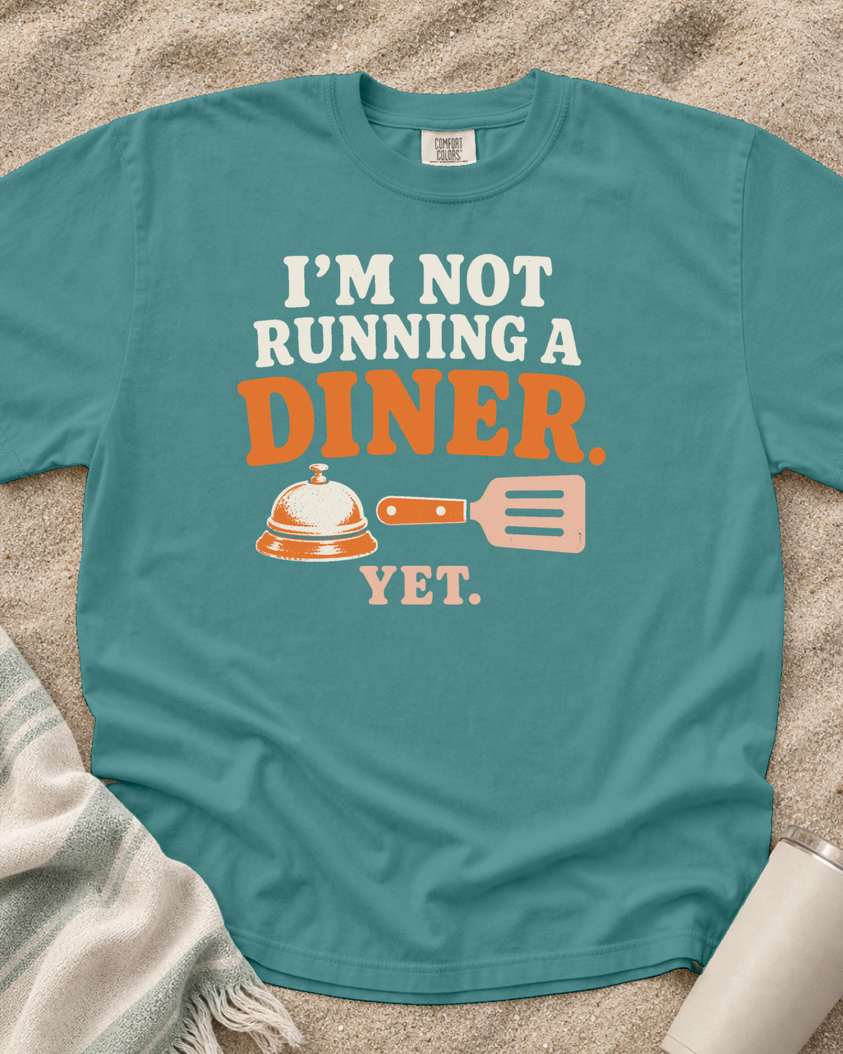 Seafoam garment-dyed tee with I’m Not Running a Diner Yet griddle graphic.