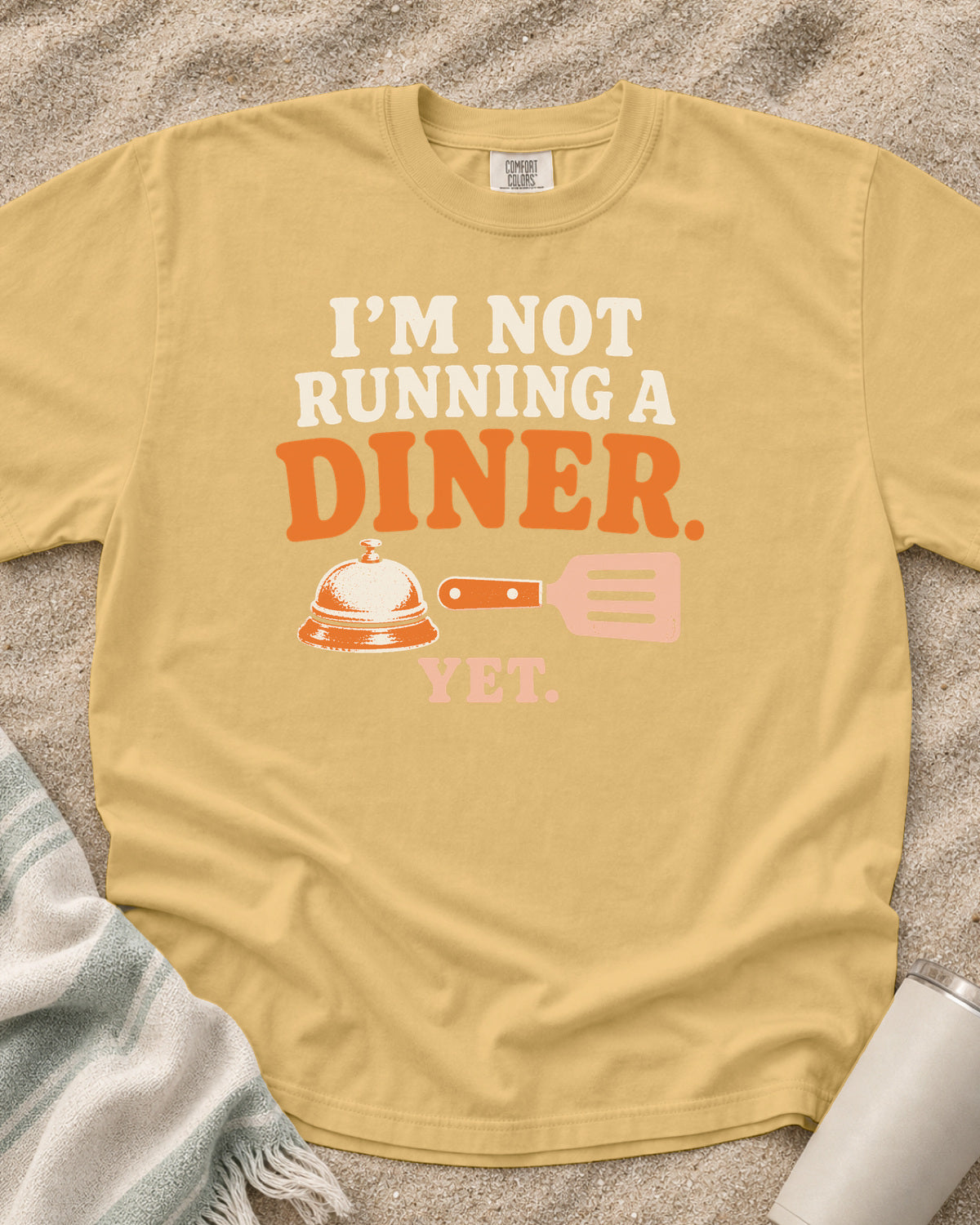 Mustard garment-dyed tee with I’m Not Running a Diner Yet griddle graphic.