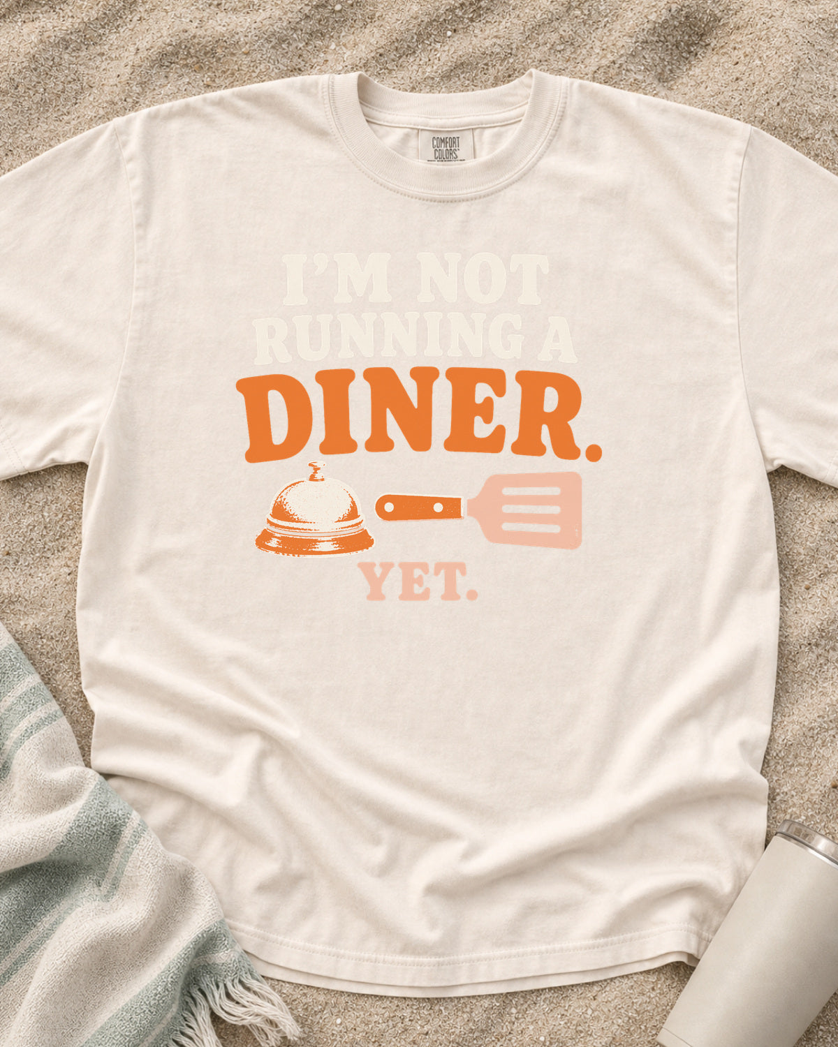 Ivory garment-dyed tee with I’m Not Running a Diner Yet griddle graphic.
