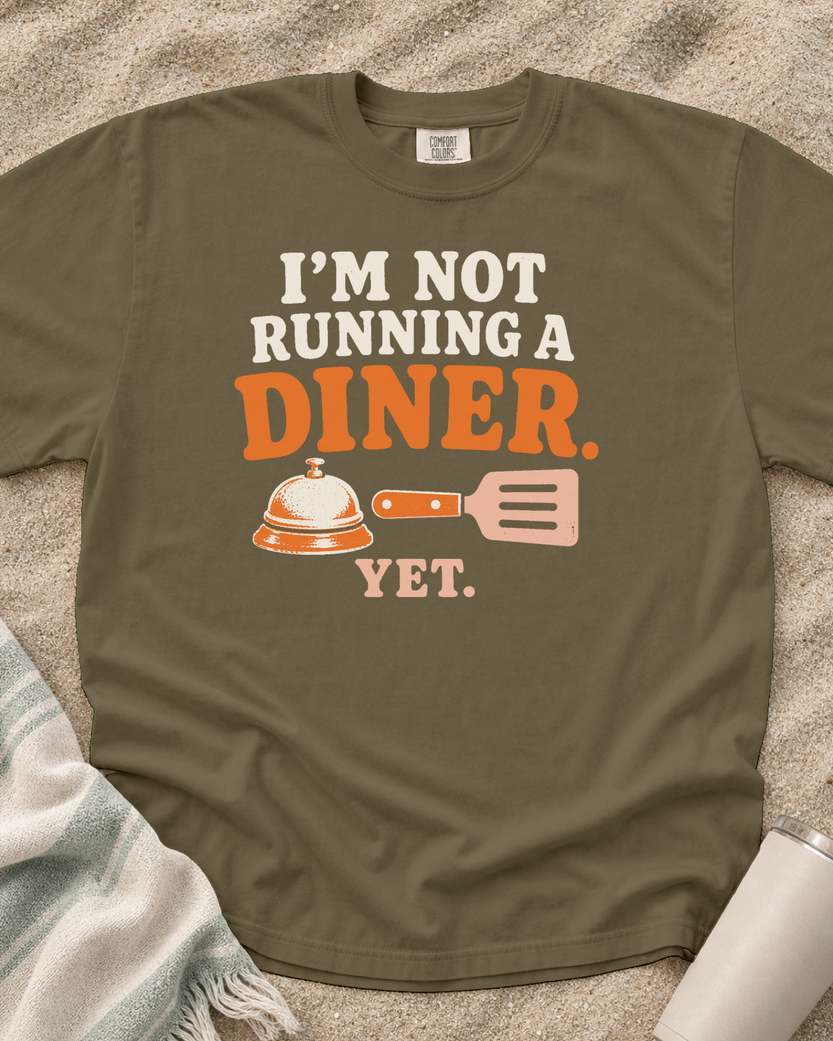 Khaki garment-dyed tee with I’m Not Running a Diner Yet griddle graphic.